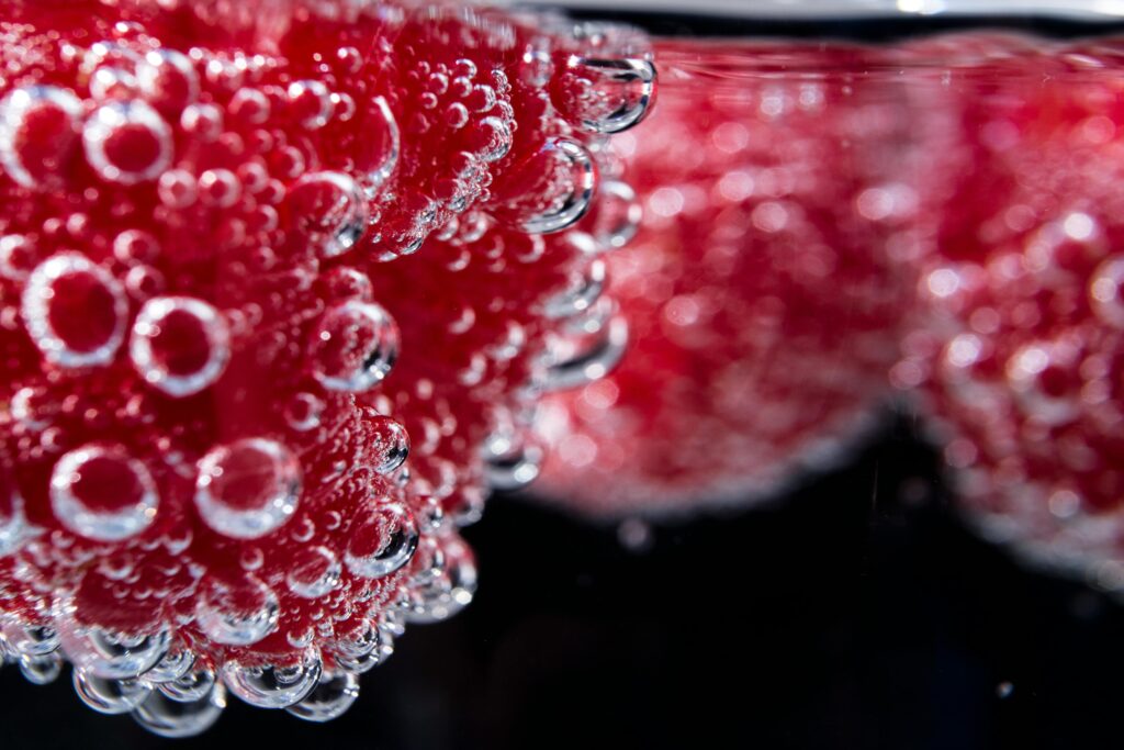 Detailed shot of vibrant red fruit with hydration bubbles in water. Fresh and juicy feel.