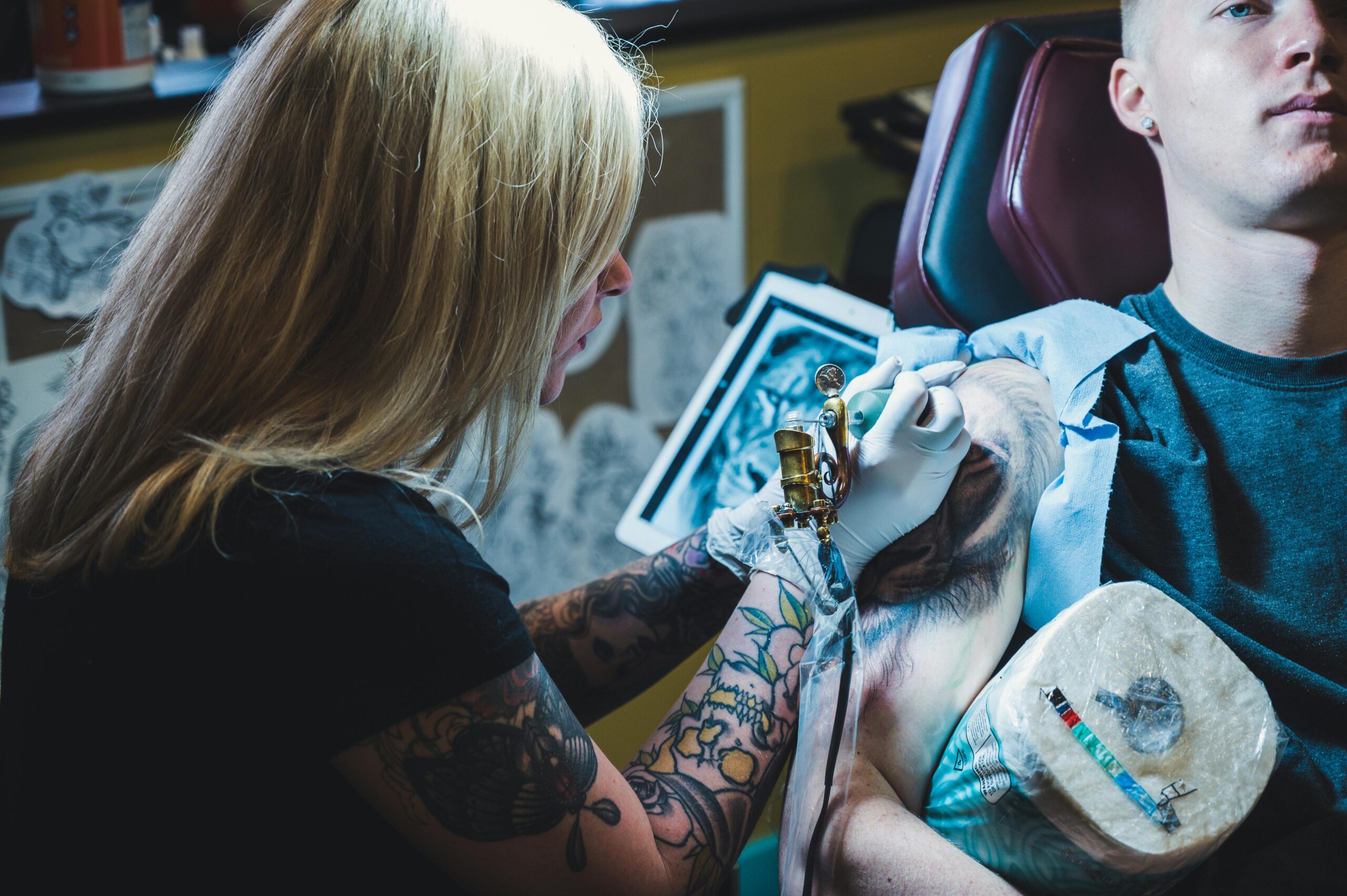 A tattoo artist concentrates while creating a detailed tattoo design on a client's arm in a studio setting.