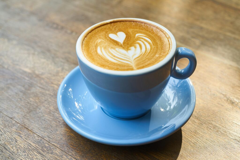 A beautifully crafted latte with heart-shaped art in a blue cup on a wooden table.