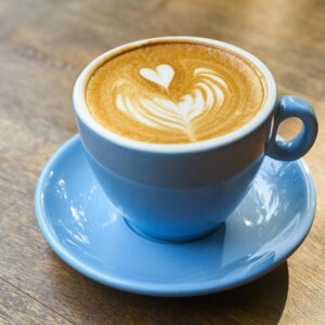 A beautifully crafted latte with heart-shaped art in a blue cup on a wooden table.
