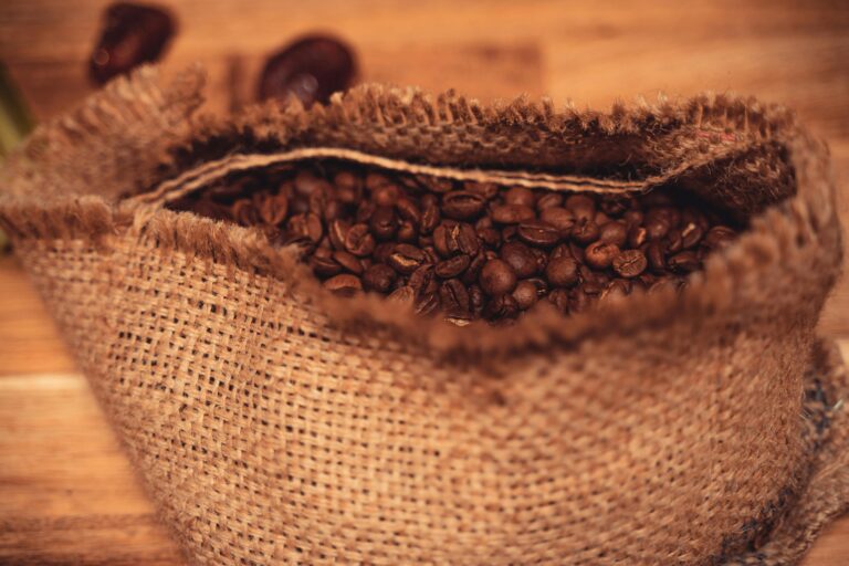 A burlap sack overflowing with freshly roasted coffee beans on a wooden surface.